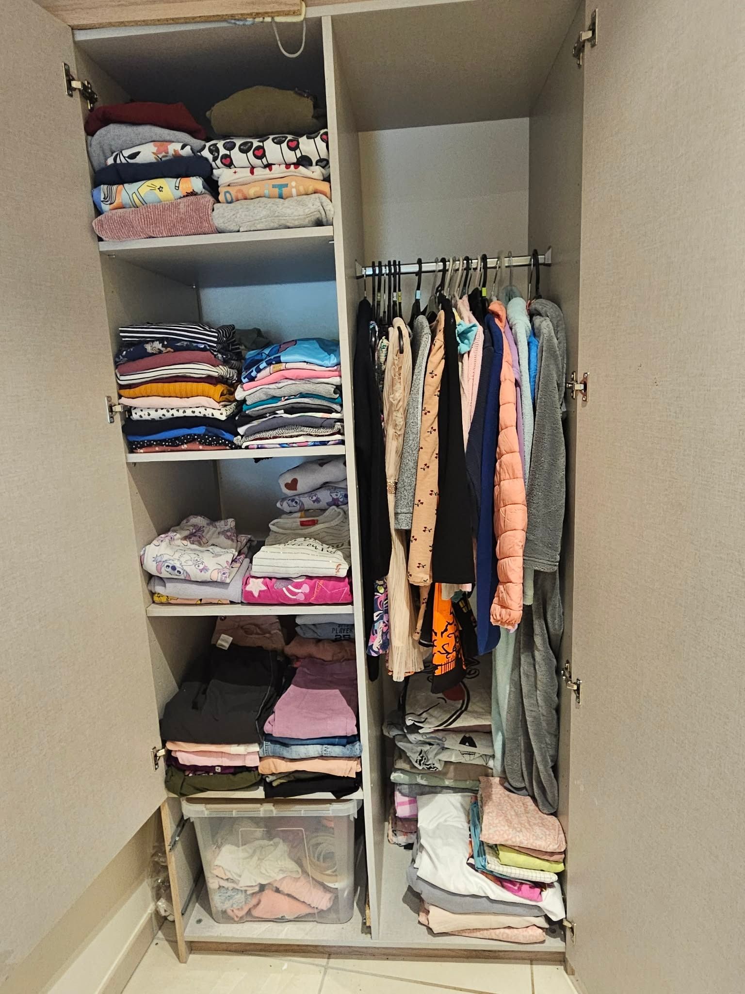 Le même placard après intervention : vêtements pliés par catégorie sur chaque étagère, penderie dégagée avec les vêtements sur cintres, bac de rangement au sol